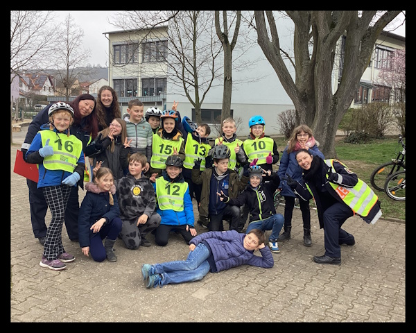 Das Bild ist ein Gruppenbild der Klasse mit Klassenlehrerin und den Damen der Verkehrspolizei. Die Kinder tragen gelbe Sicherheitswesten.